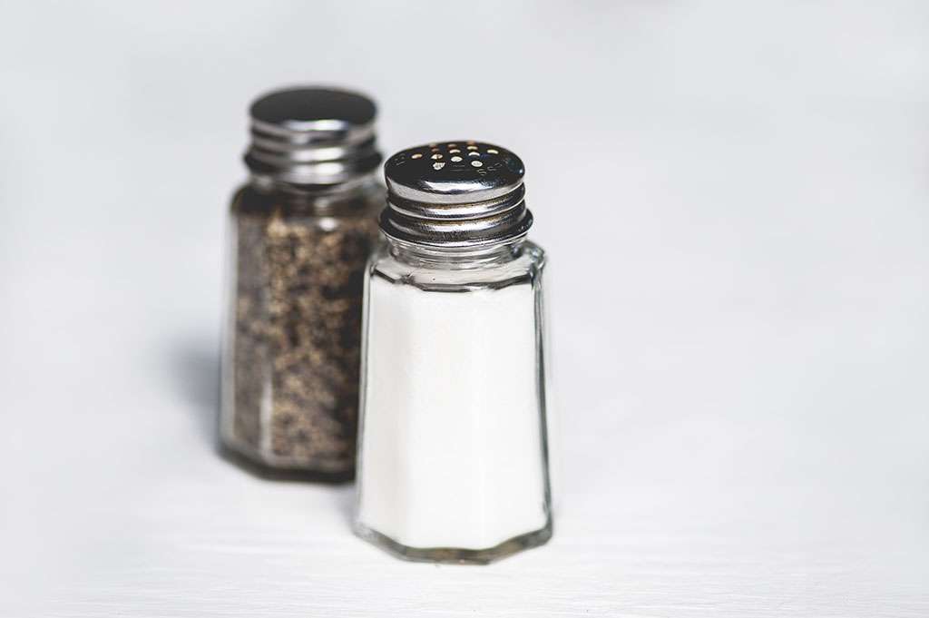 Macro view of salt and pepper shakers on rustic wooden table; shallow DOF